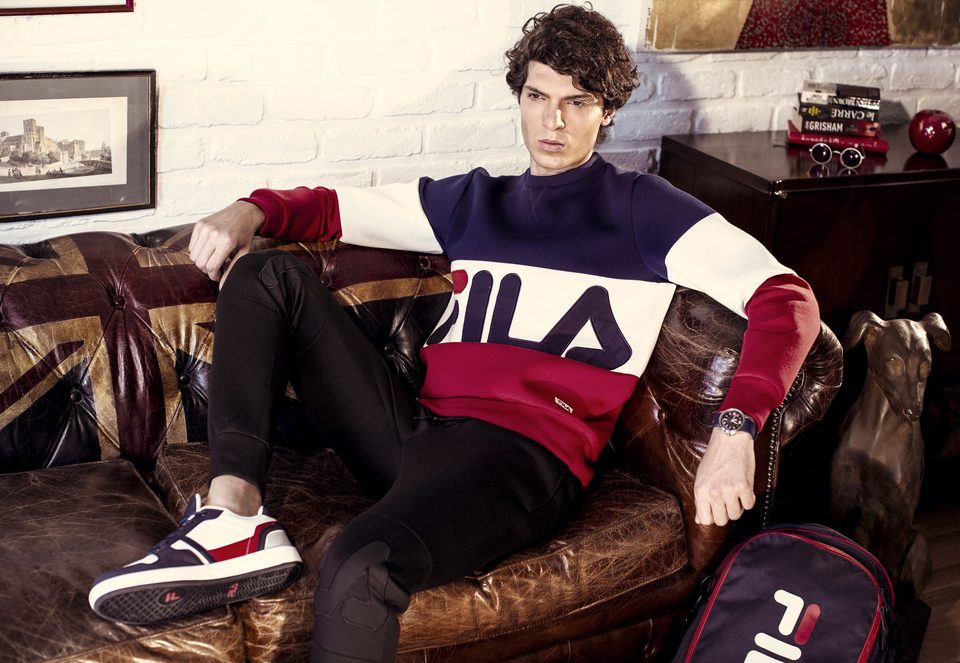 A model in a FILA colour-block sweatshirt lounges on a worn leather sofa