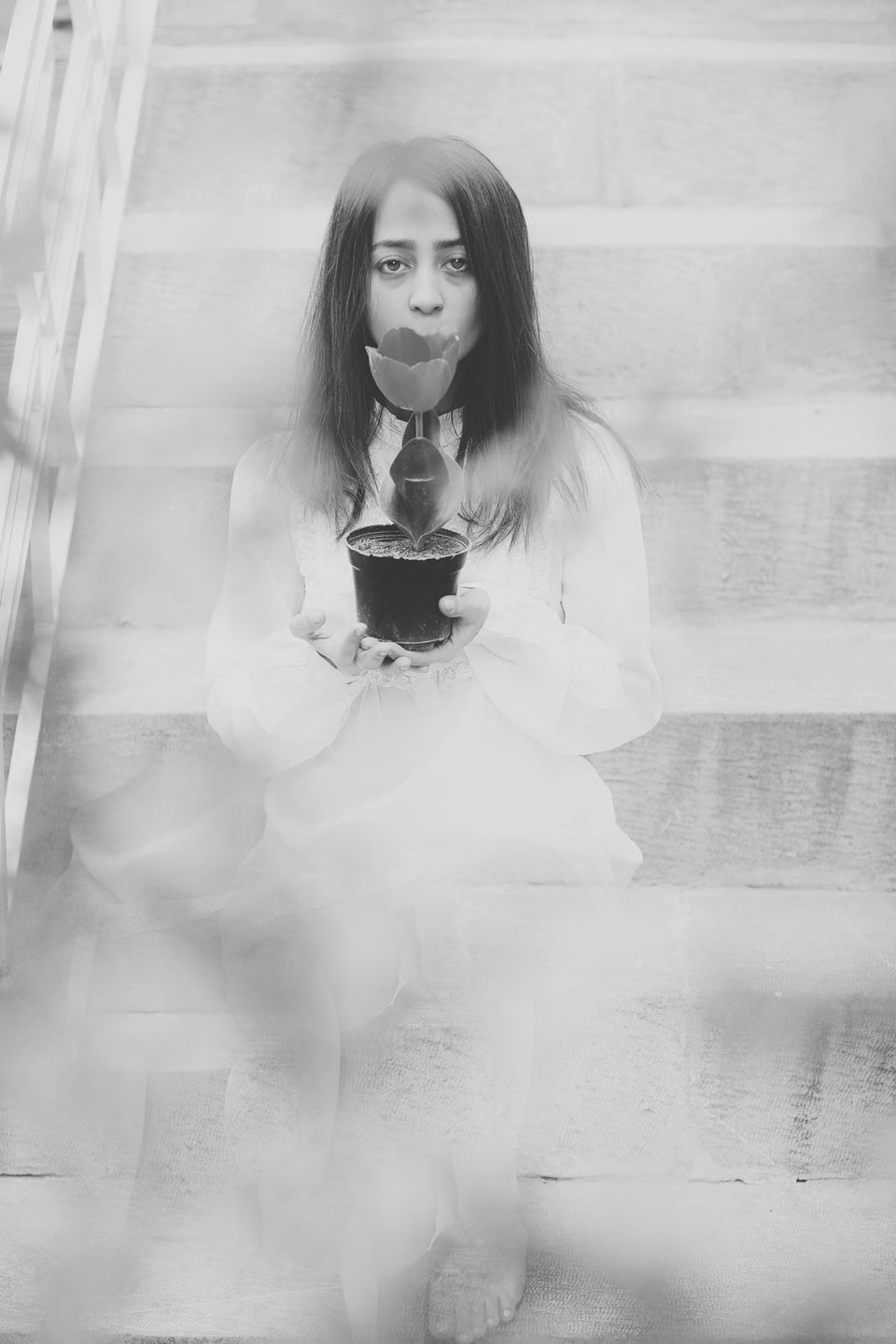 Faded black-and-white collage of a young woman holding a cup on a pale staircase