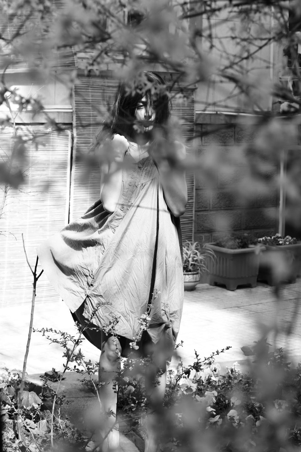 A woman in a pale dress half hidden by foliage in a garden, black and white
