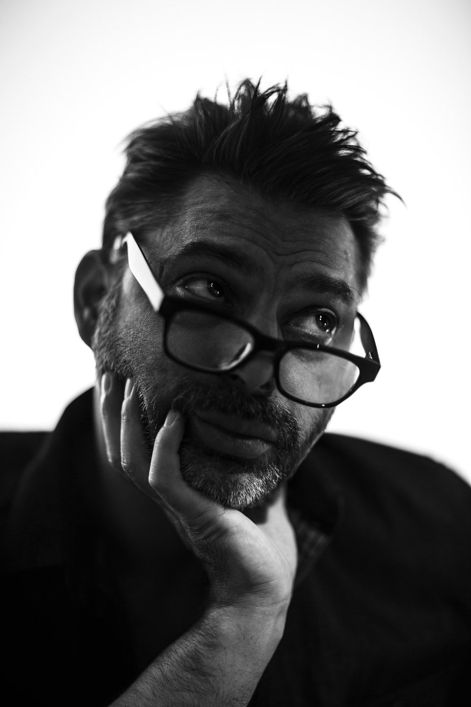 Payman Maadi with glasses pushed onto his forehead, chin resting on his hand, black and white