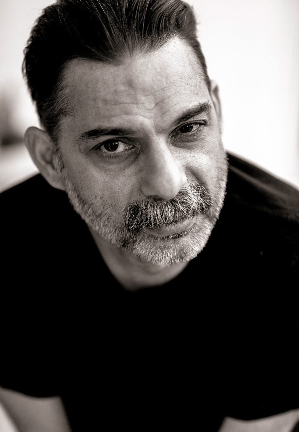 Close portrait of Payman Maadi in a black T-shirt, looking down into the camera