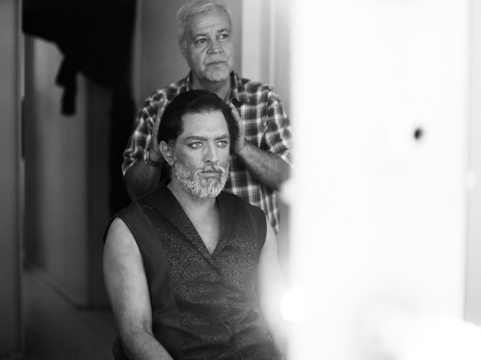 Actor Bahram Radan in costume and makeup backstage, a makeup artist standing behind him