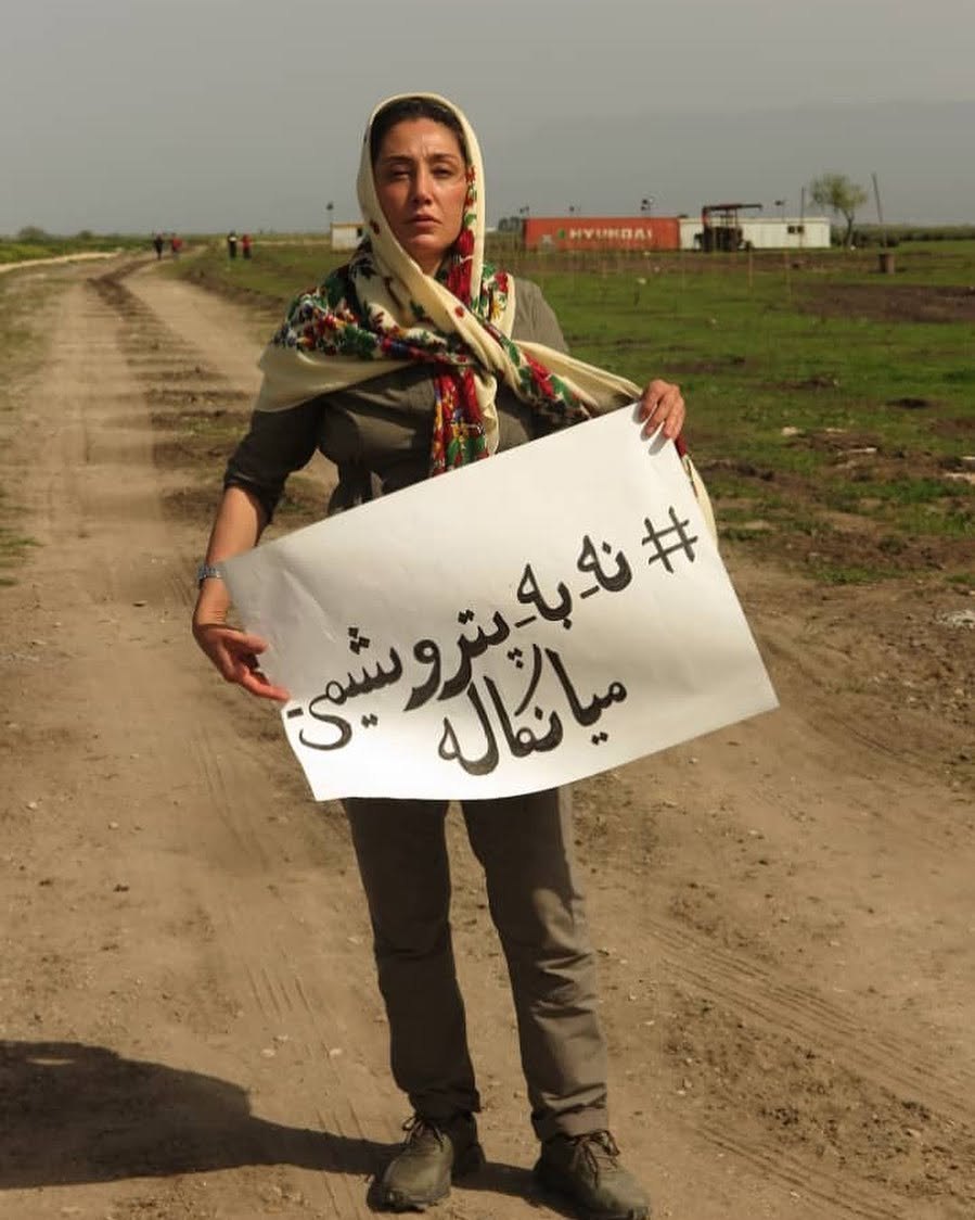 Hedieh Tehrani on a dirt road holding a handwritten sign in Persian: no to the Miankaleh petrochemical plant