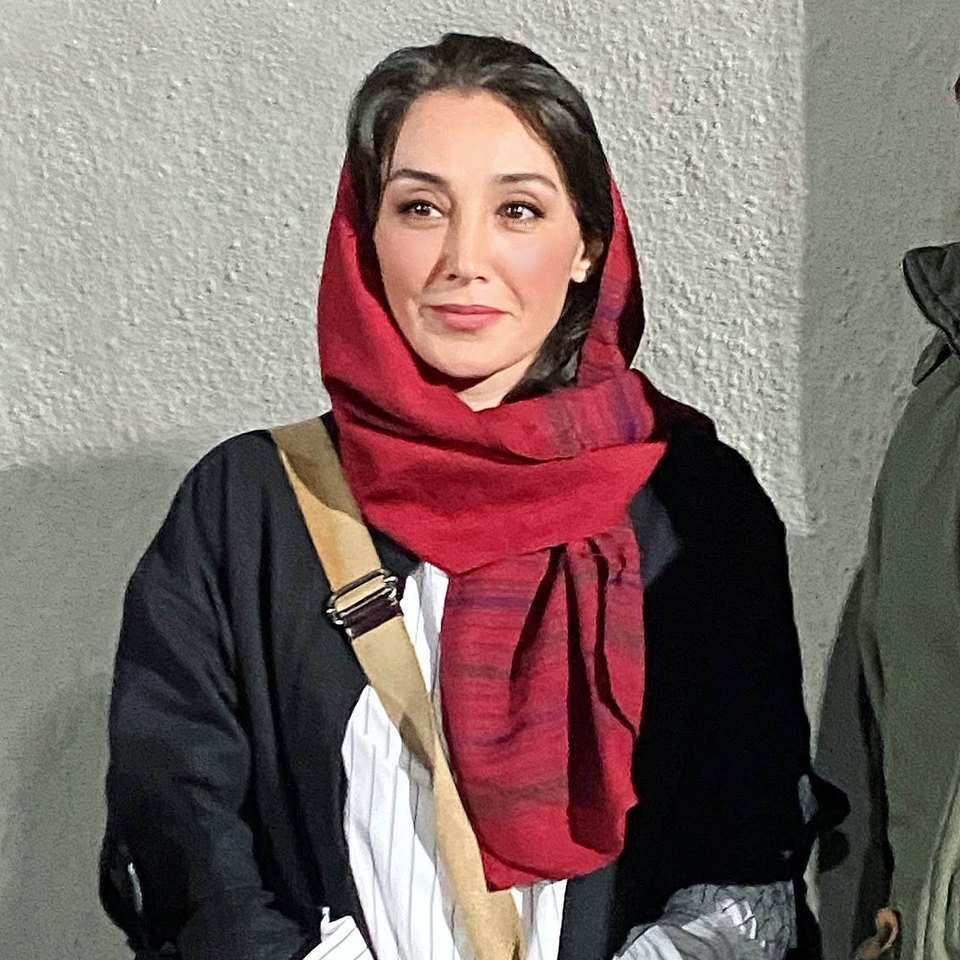 Portrait of Hedieh Tehrani in a red headscarf and dark coat against a pale textured wall