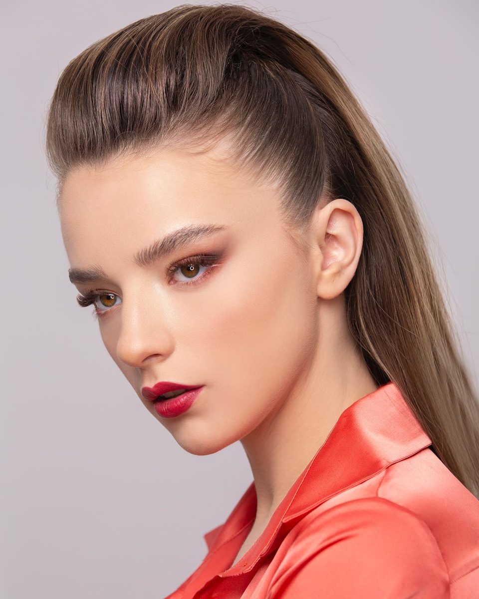 A woman with a high ponytail and red lips in a coral satin shirt