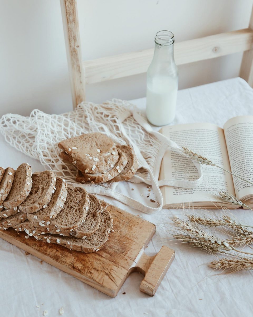 Sliced bread on a board with a bottle of milk and a string bag