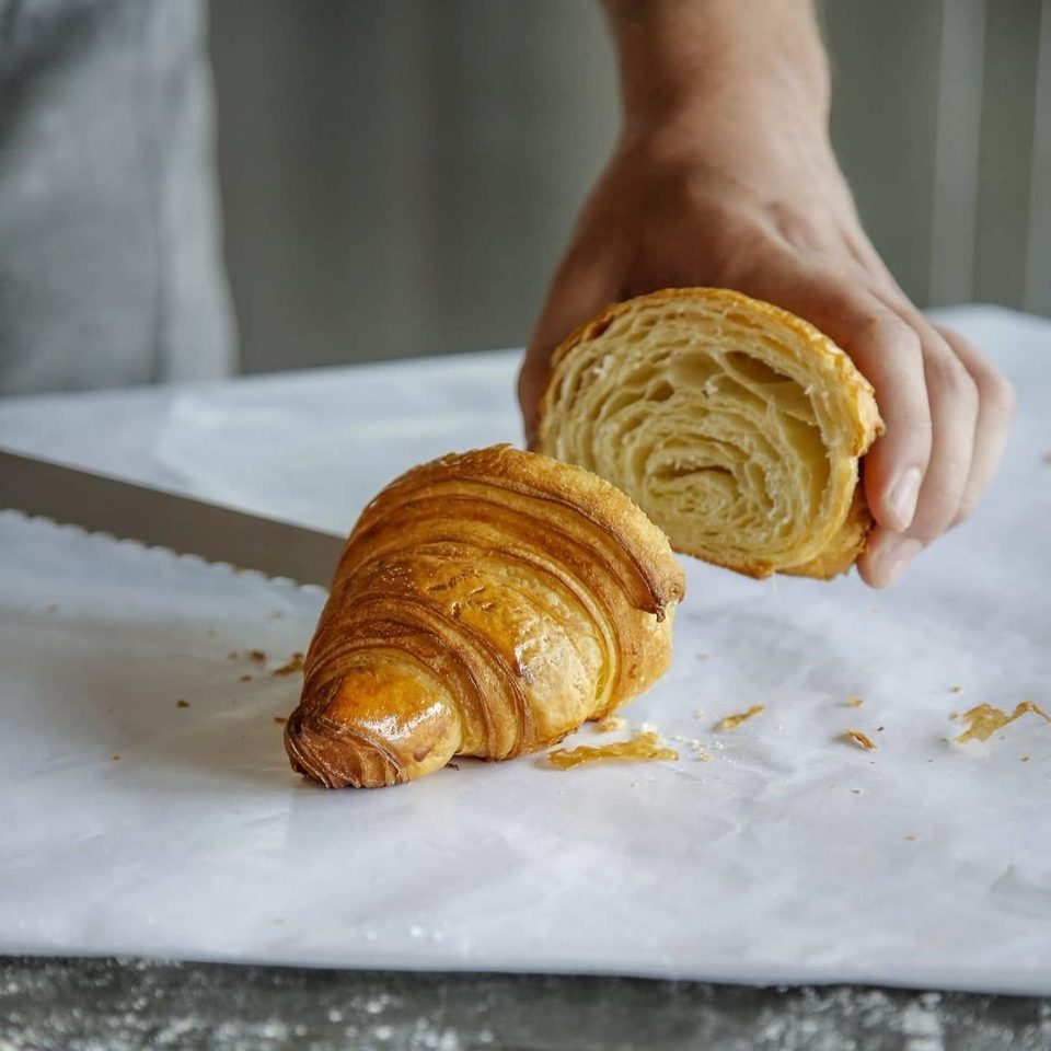 A baker cuts a croissant with a serrated knife on white paper